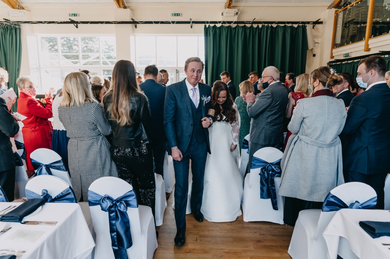 Just married couple walking down the aisle at Myddfai Community Hall as guests cheer and applaud