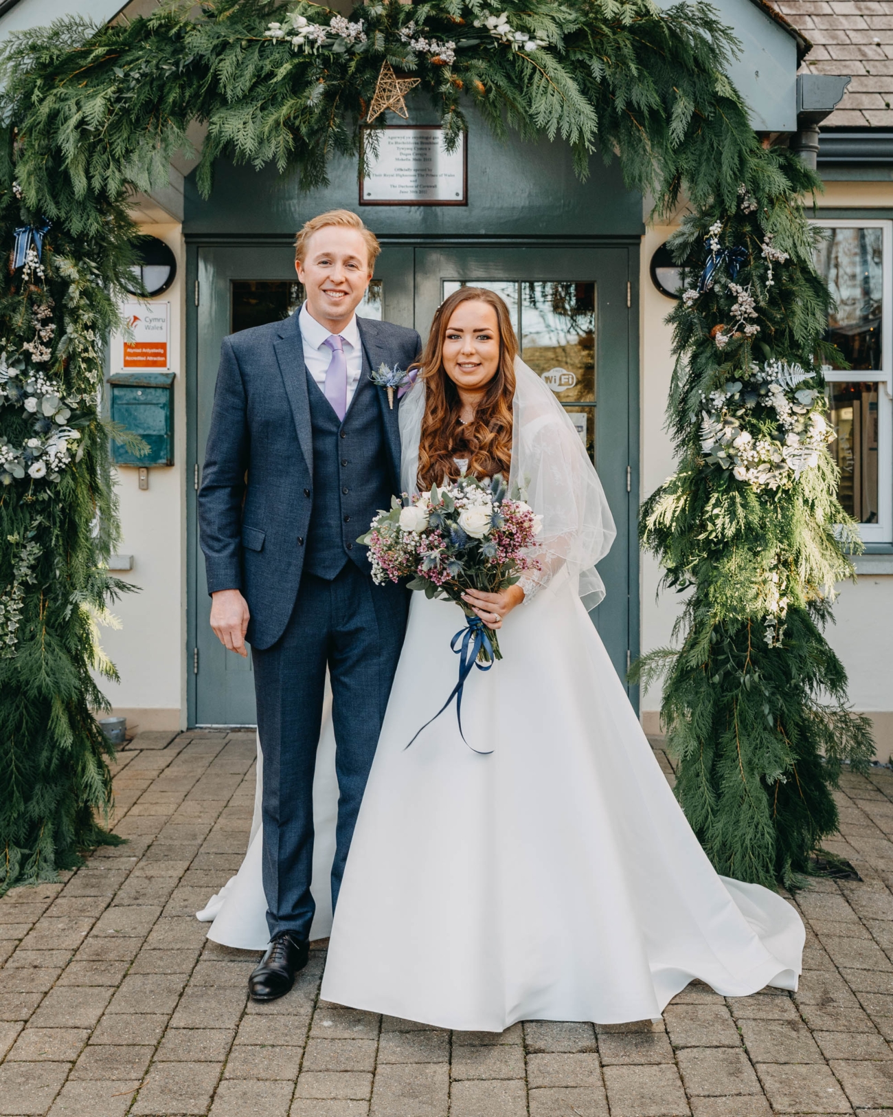 Bride and groom standing in front of Myddfai Community Hall after their wedding ceremony in Wales