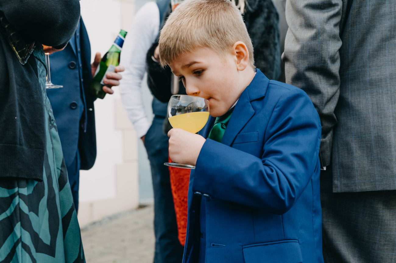 Young wedding guest sipping orange juice from a wine glass – candid moment captured at a wedding in Myddfai