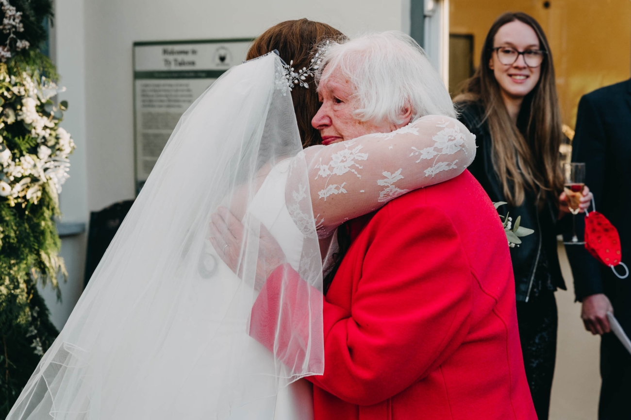 Bride embracing an elderly guest in an emotional moment outside Myddfai Community Hall – captured by a candid wedding photographer
