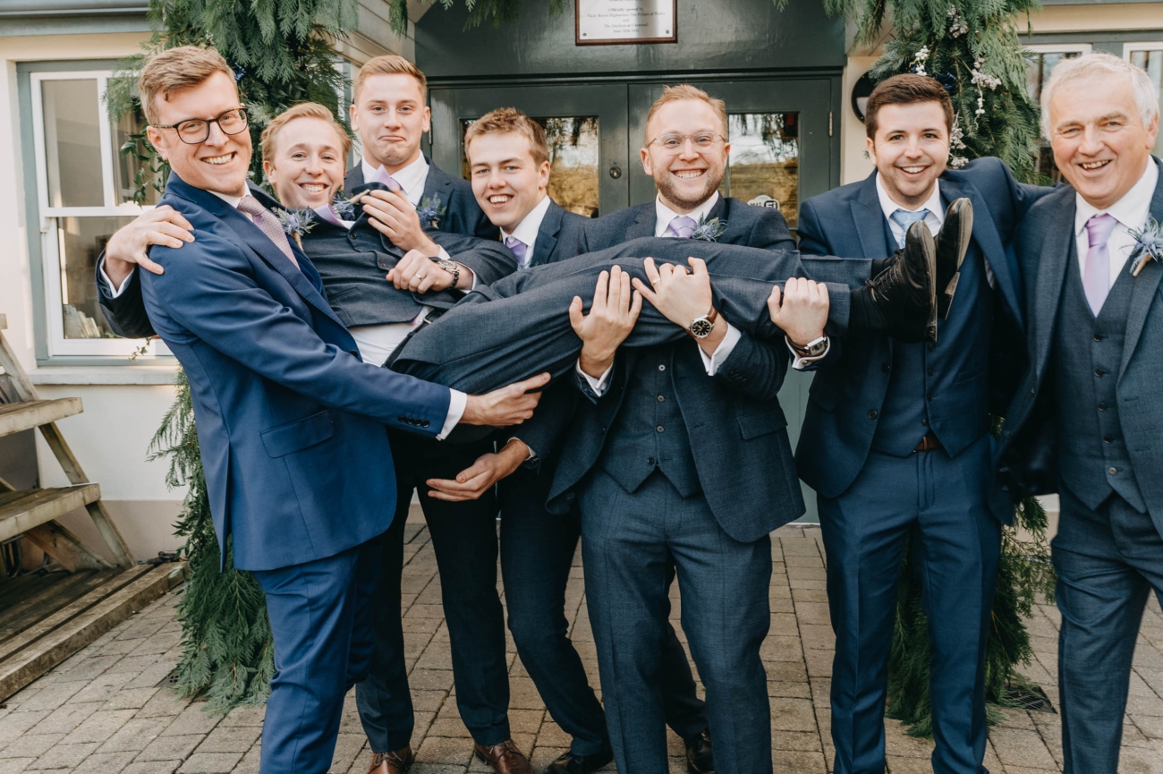 Groomsmen lifting the groom outside Myddfai Community Hall – fun and candid wedding group photo