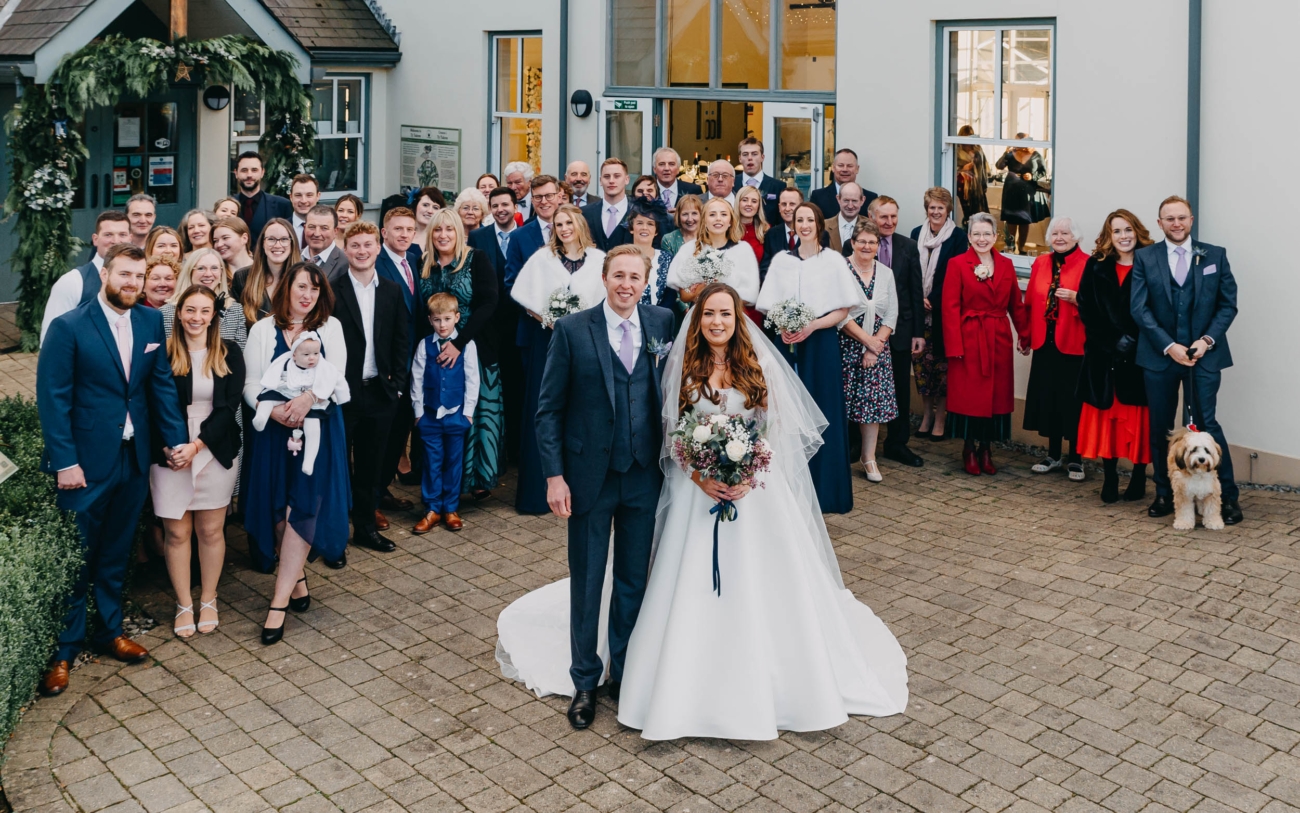 Full group photo of wedding guests with the couple in front of Myddfai Community Hall – a joyful moment from the celebration