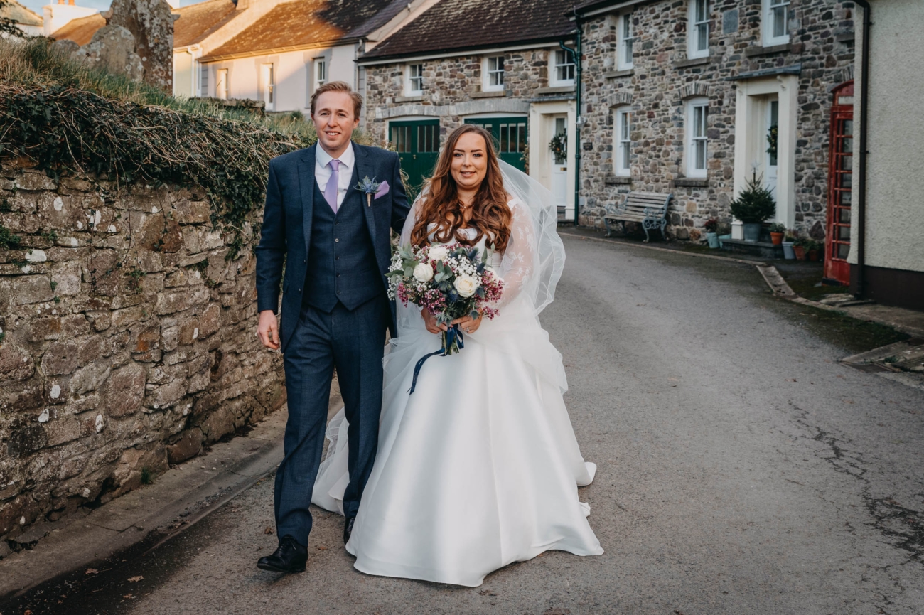 Bride and groom smiling as they walk through the village of Myddfai after their wedding ceremony