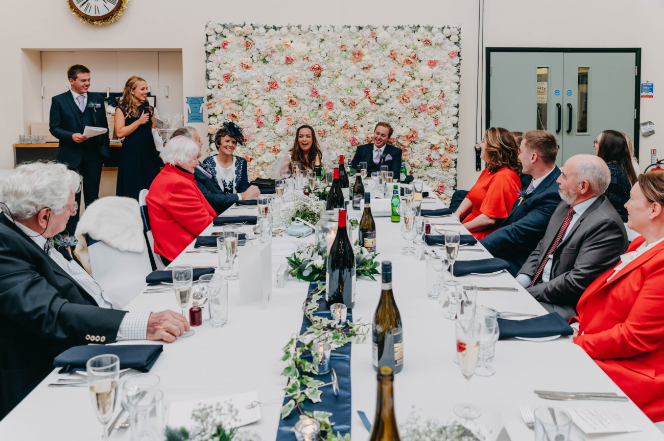 Wedding guests listening to a joint speech during the reception at Myddfai Community Hall – candid and joyful atmosphere