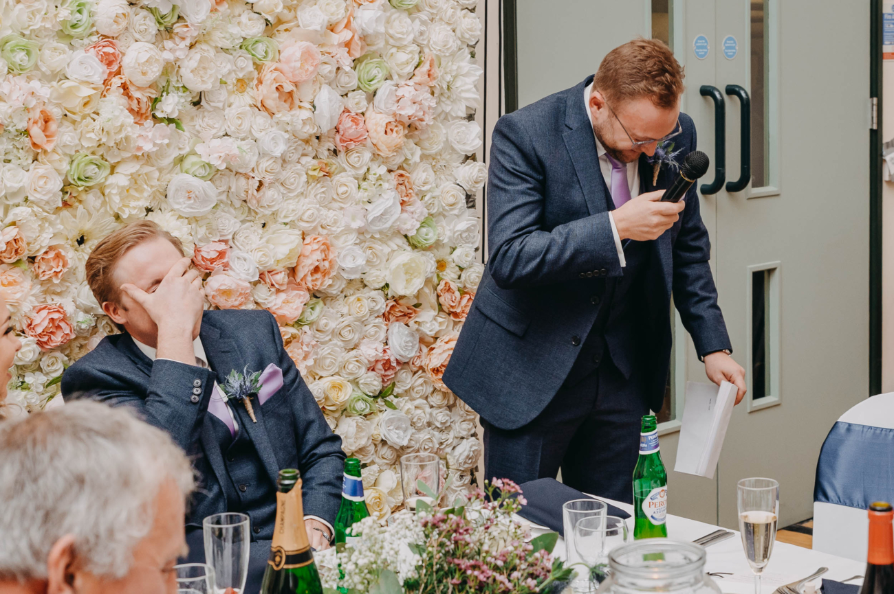 Groom laughing with his face in hand during a wedding speech at Myddfai Community Hall – a truly candid moment