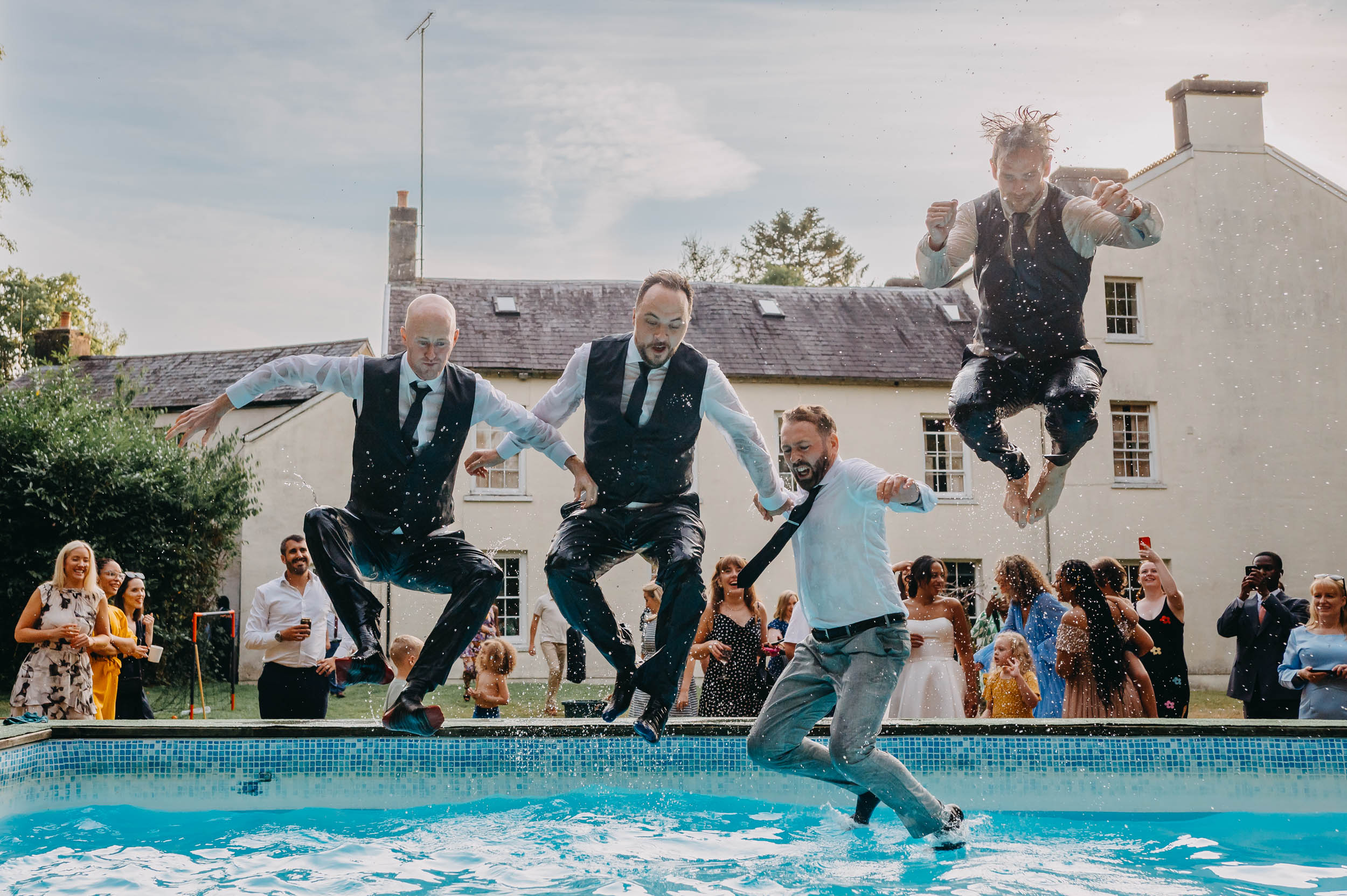wedding guests jumping into a pool during a lively outdoor wedding reception full of energy and chaos