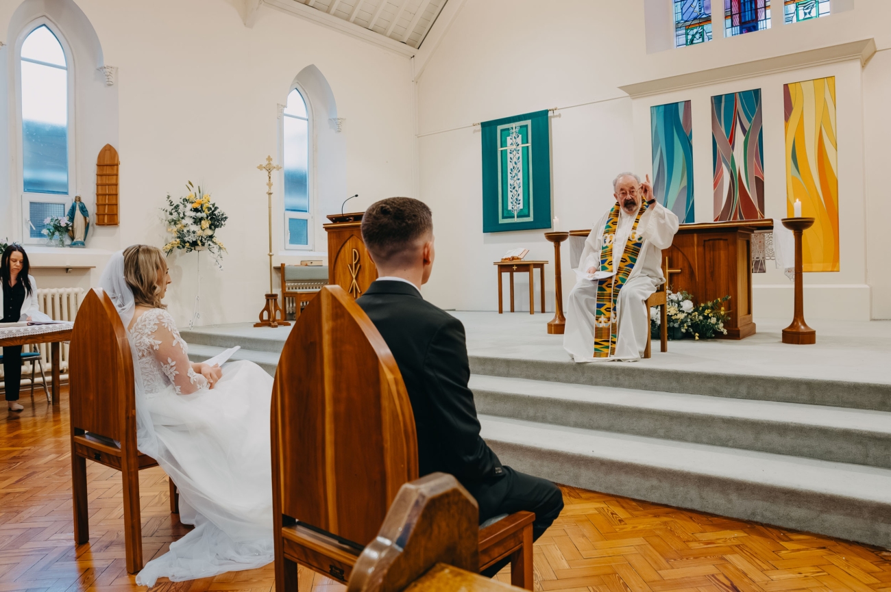 relaxed church wedding ceremony with priest speaking and couple seated, documentary wedding photography Cardiff