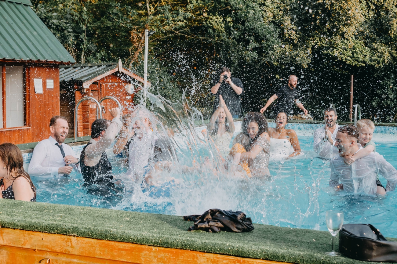 wedding guests splashing water in a pool during a chaotic and joyful candid wedding moment