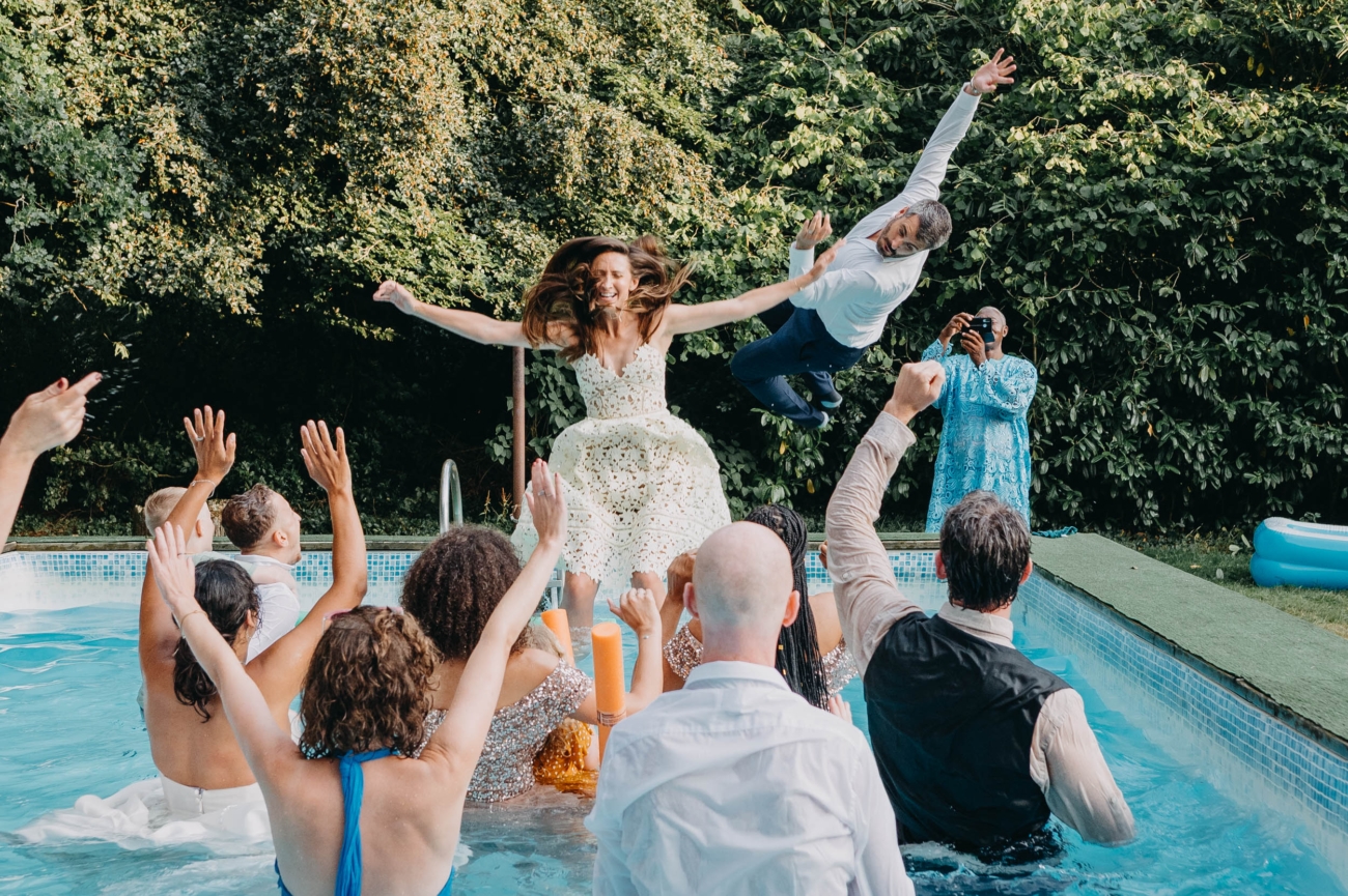 wedding guests mid-air jumping into a pool during a spontaneous high-energy outdoor wedding moment