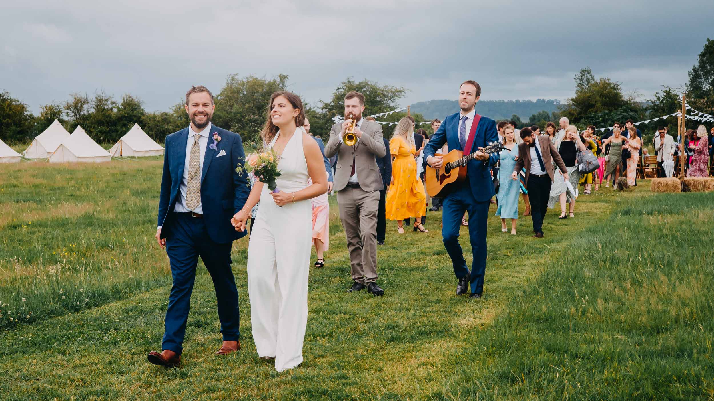 couple walking with guests during festival wedding in Glastonbury Somerset countryside