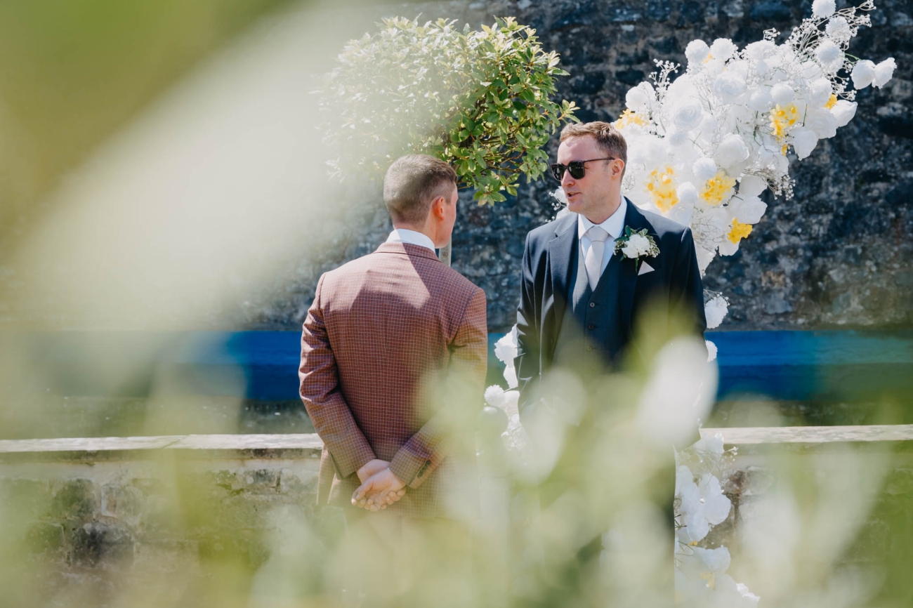 Groom talking with a guest beside the floral ceremony arch in the Italian Gardens