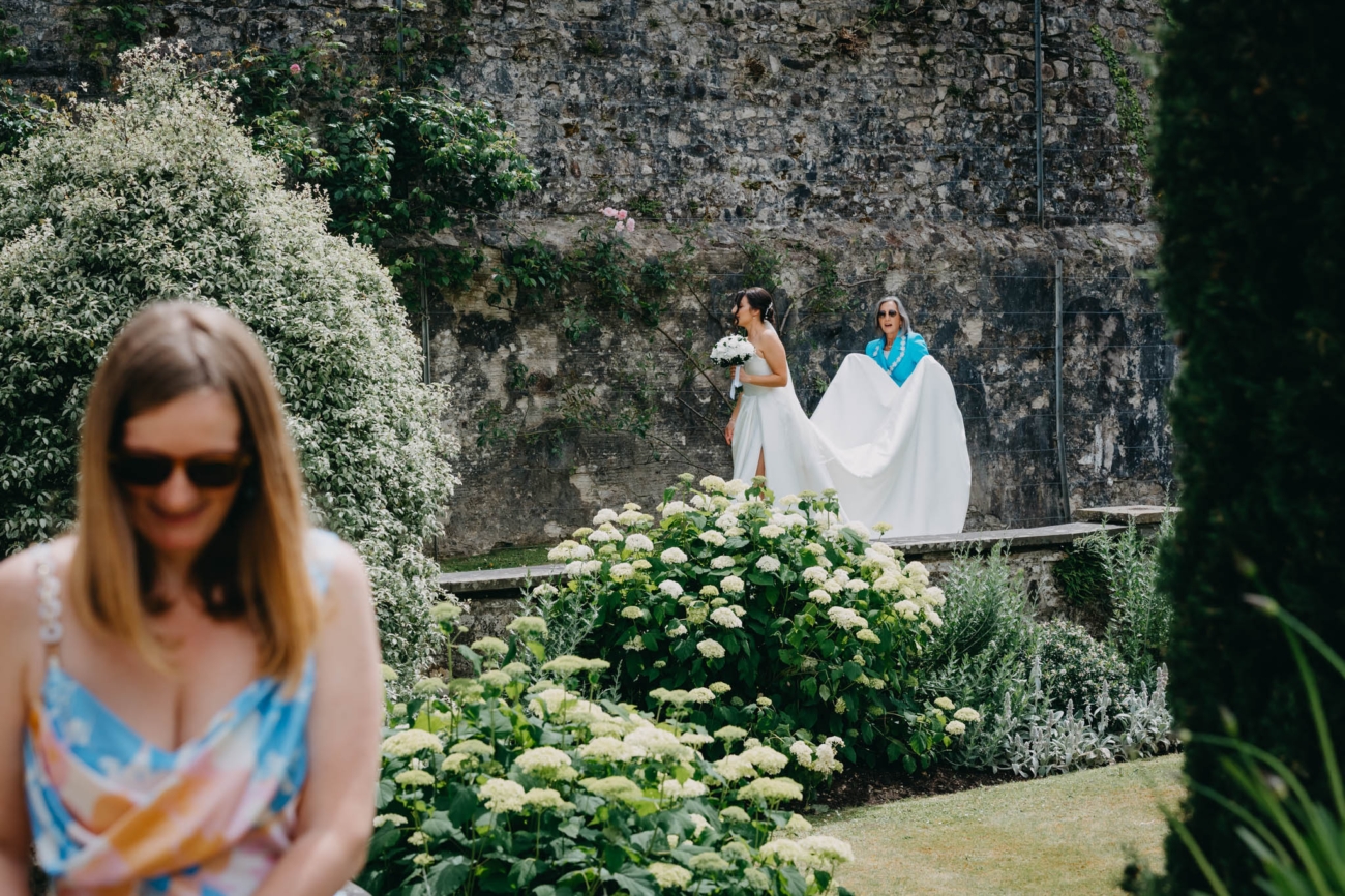Bride walking through the Italian Gardens while a wedding guest carries her dress train before the ceremony