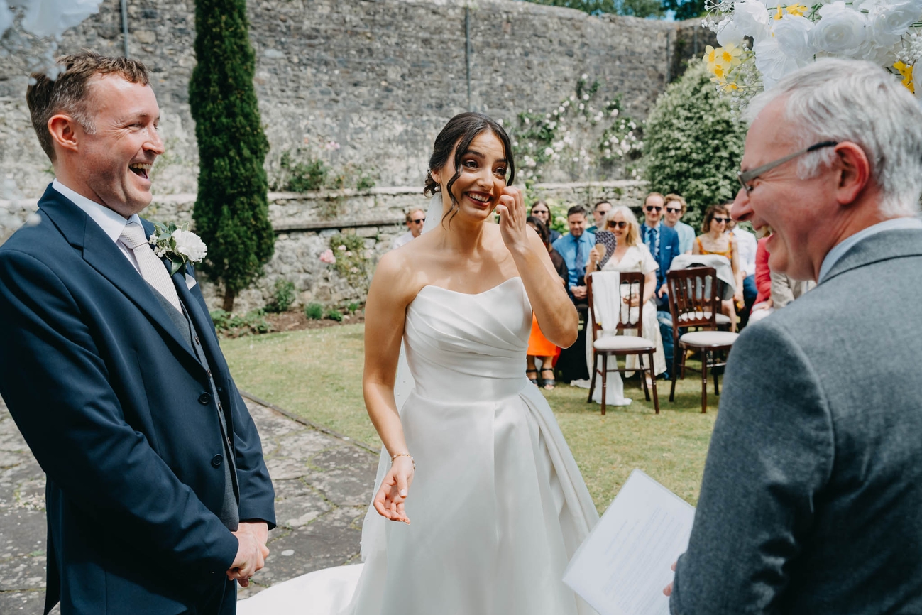 Bride and groom laughing with their celebrant during an outdoor wedding ceremony in the Italian Gardens at St Fagans
