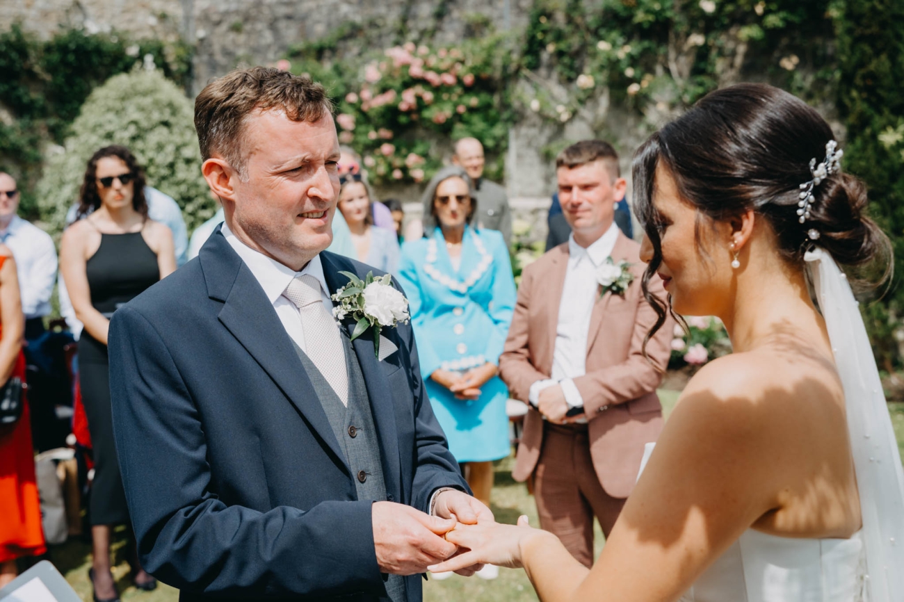Groom placing a wedding ring on the bride’s finger during their outdoor ceremony