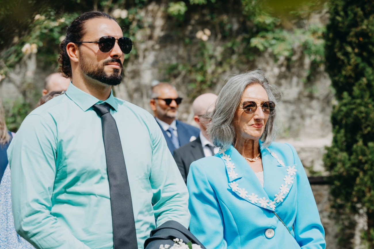Two wedding guests watching the outdoor ceremony in the summer sunshine at St Fagans