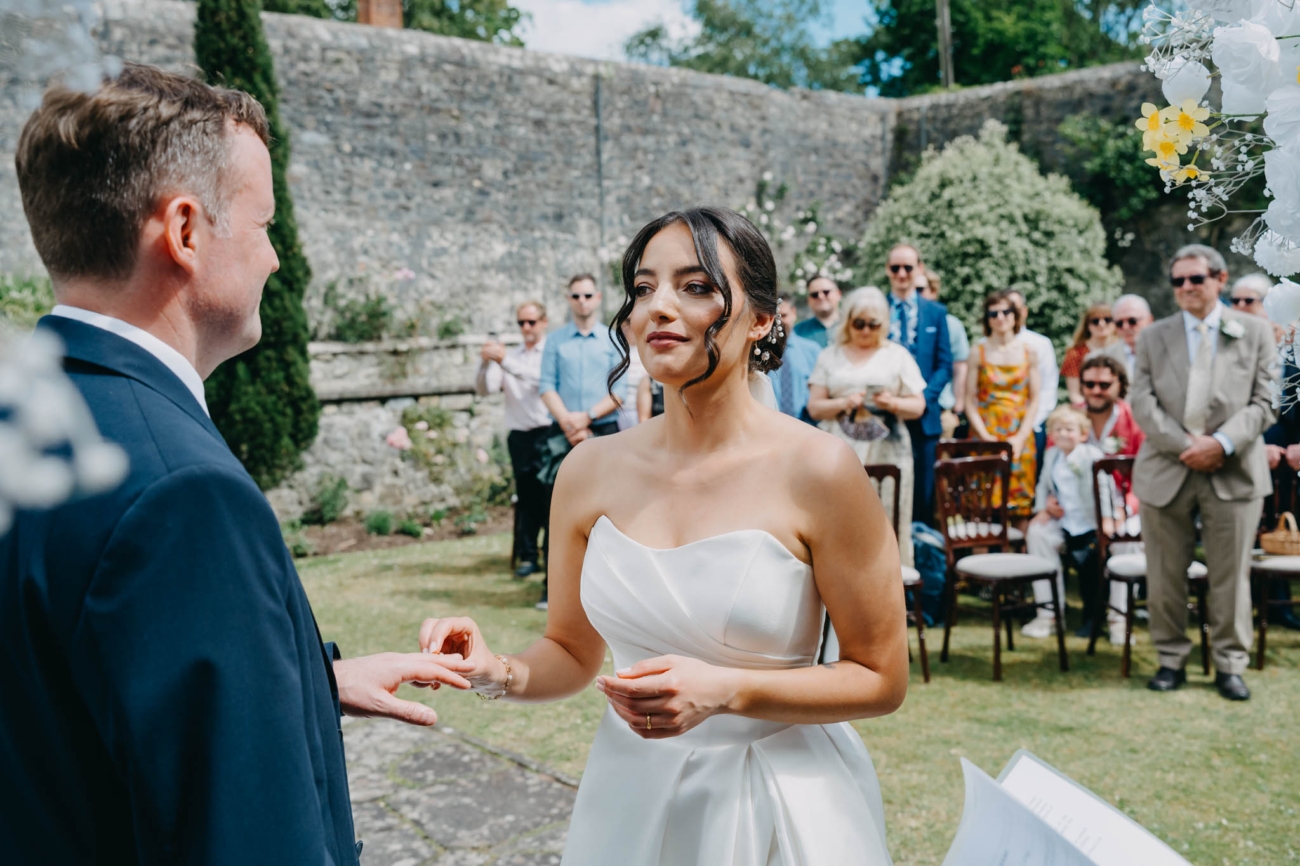 Bride placing a wedding ring on the groom’s finger as their guests watch