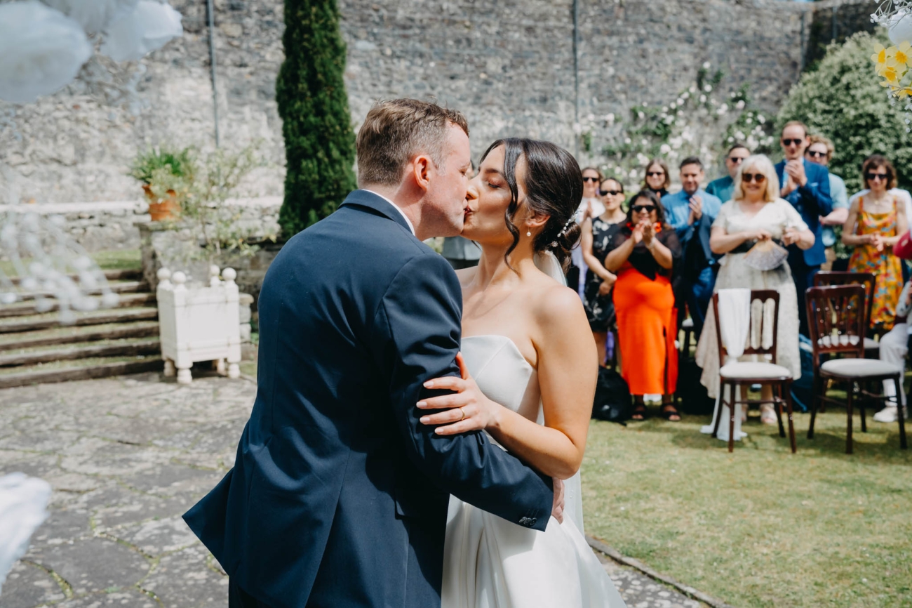 Bride and groom sharing their first kiss as wedding guests applaud in the Italian Gardens