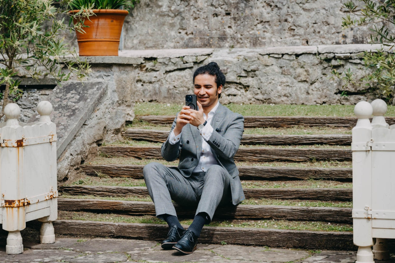 Wedding guest taking a photograph with his phone while seated on the garden steps