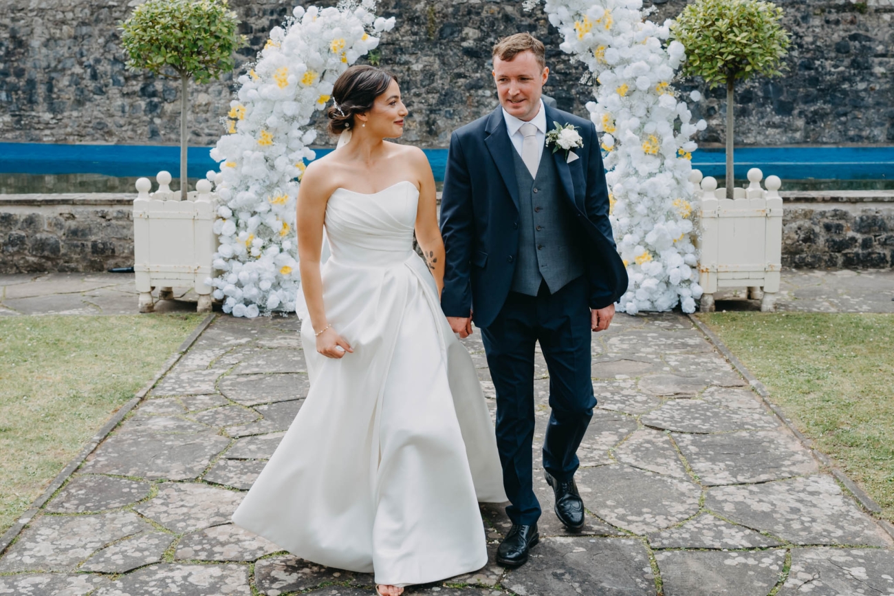 Bride and groom holding hands as they walk away from the floral arch after their ceremony