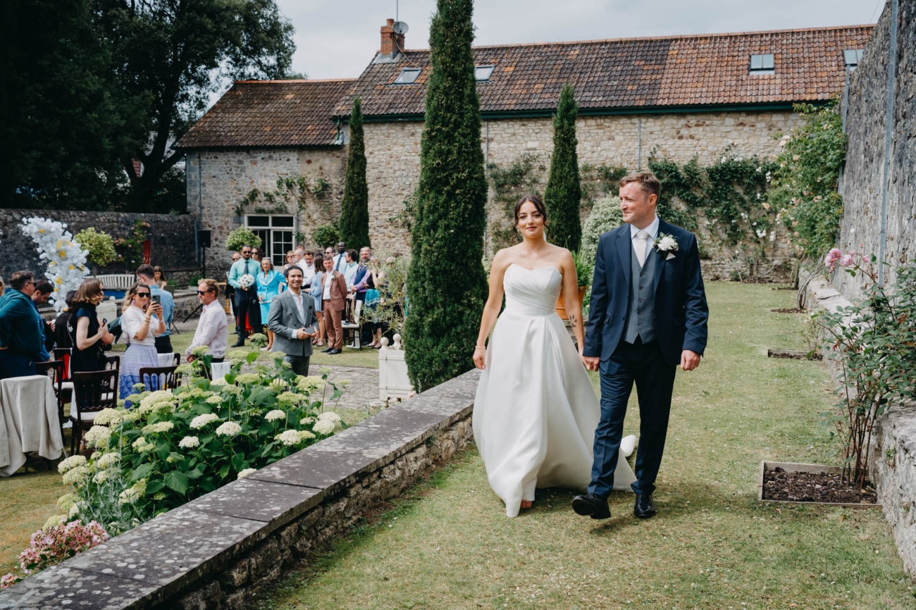 Newlyweds walking through the Italian Gardens as their wedding guests watch
