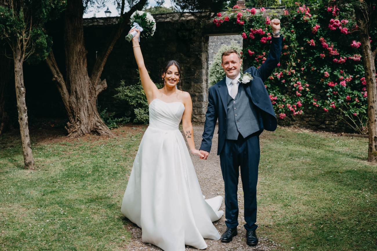 Newlyweds raising their arms in celebration after an outdoor wedding ceremony in the Italian Gardens at St Fagans