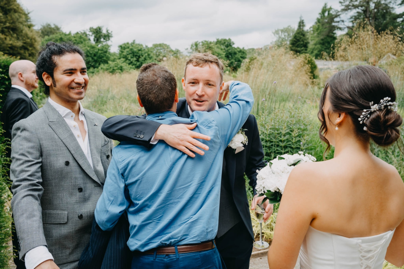 Groom being congratulated by a wedding guest as the bride watches in the Italian Gardens