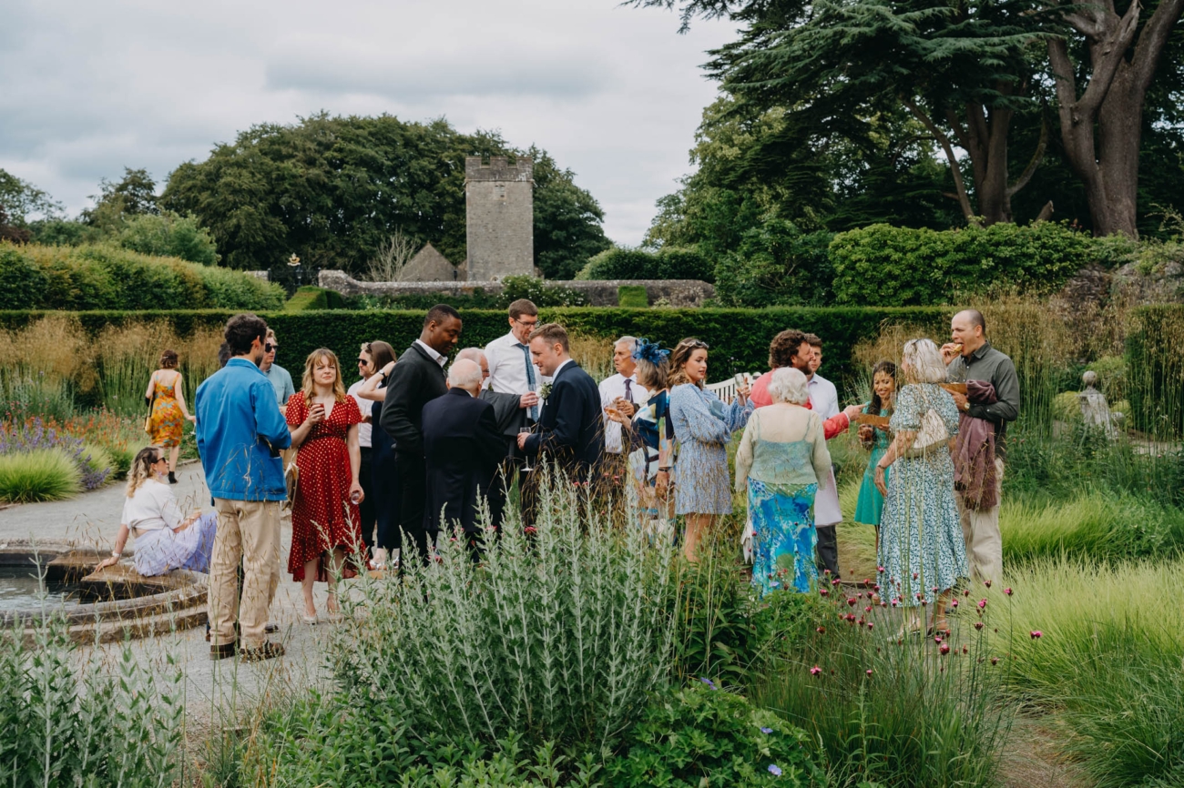 Wedding guests mingling beside the landscaped pond during post-ceremony drinks in the Italian Gardens