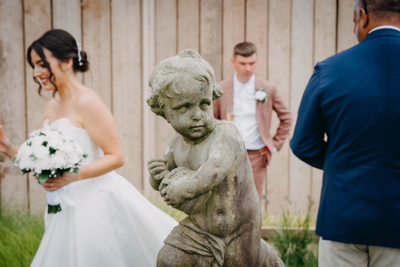 Stone garden statue in the foreground as the bride and wedding guests gather at St Fagans