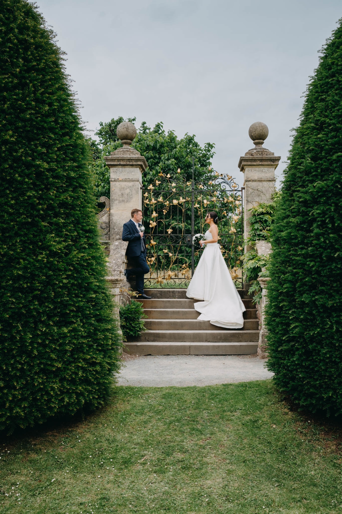 Bride and groom standing beside an ornate gate framed by tall hedges in the Italian Gardens at St Fagans