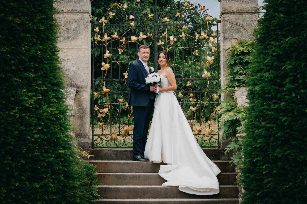 Bride and groom standing together on the steps in front of an ornate garden gate at St Fagans
