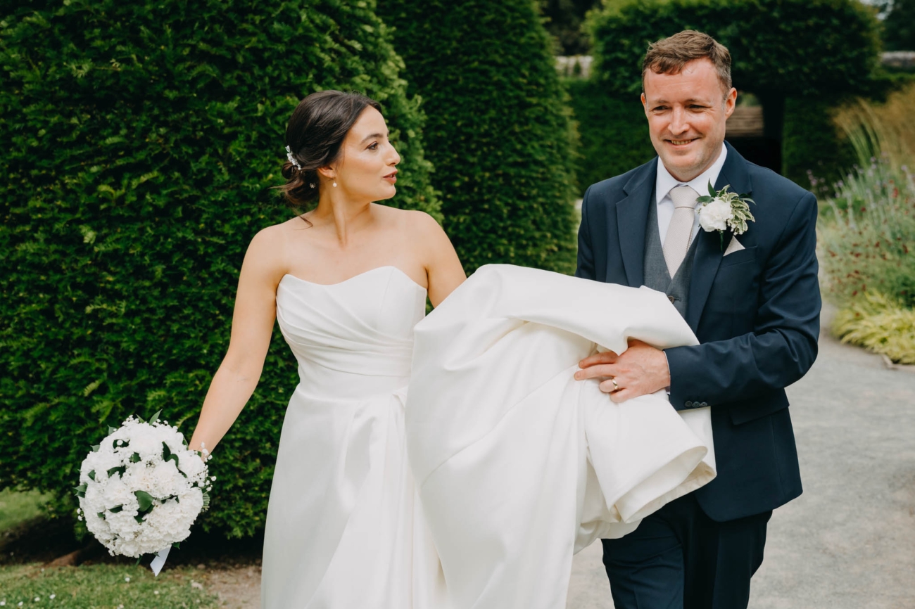 Groom carrying the bride’s dress train as they walk together through the Italian Gardens