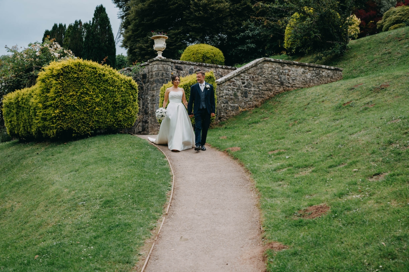 Newlyweds holding hands as they walk along a curved path through the museum gardens