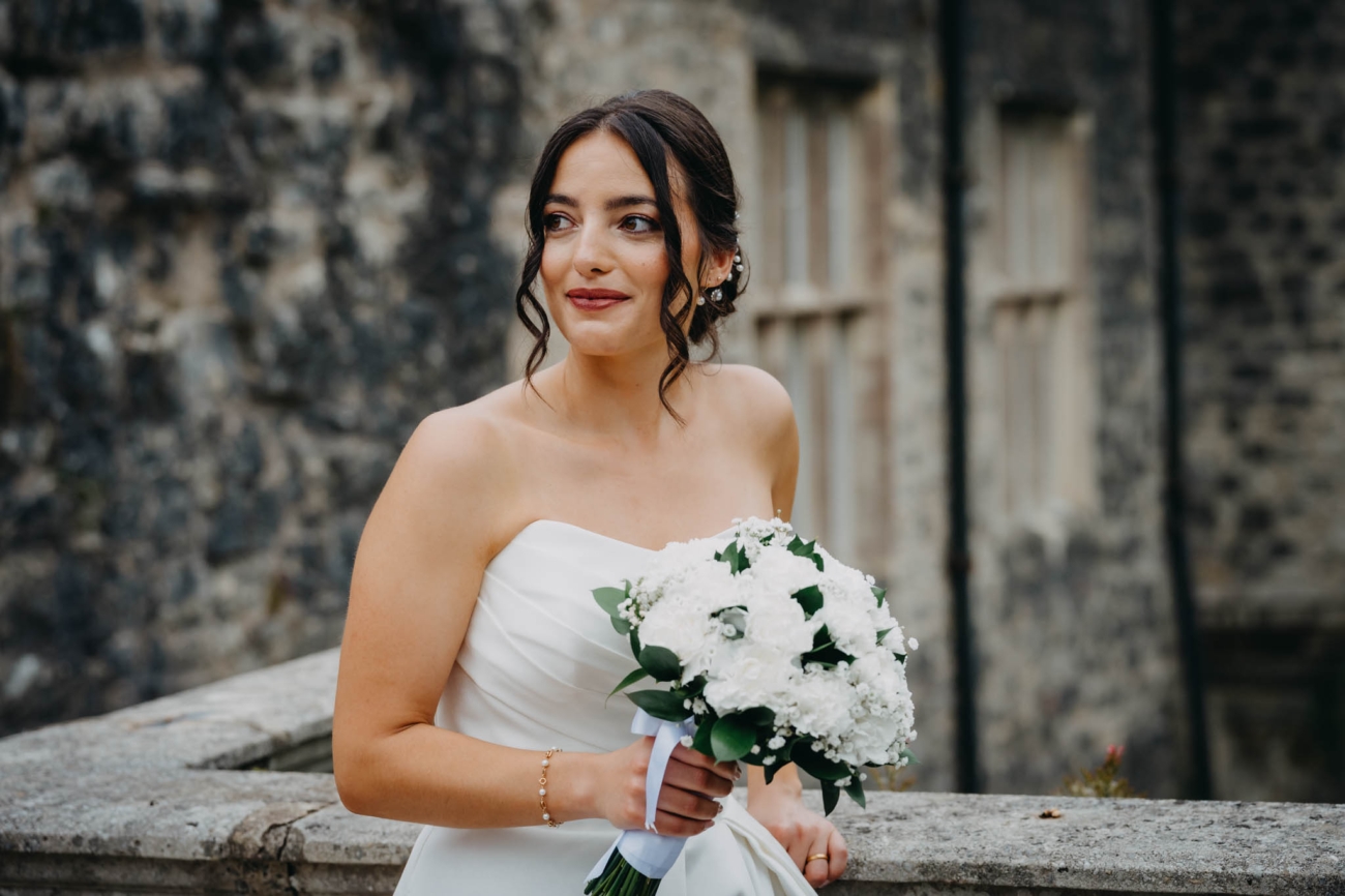 Bride holding her white bouquet in front of a historic stone building at St Fagans