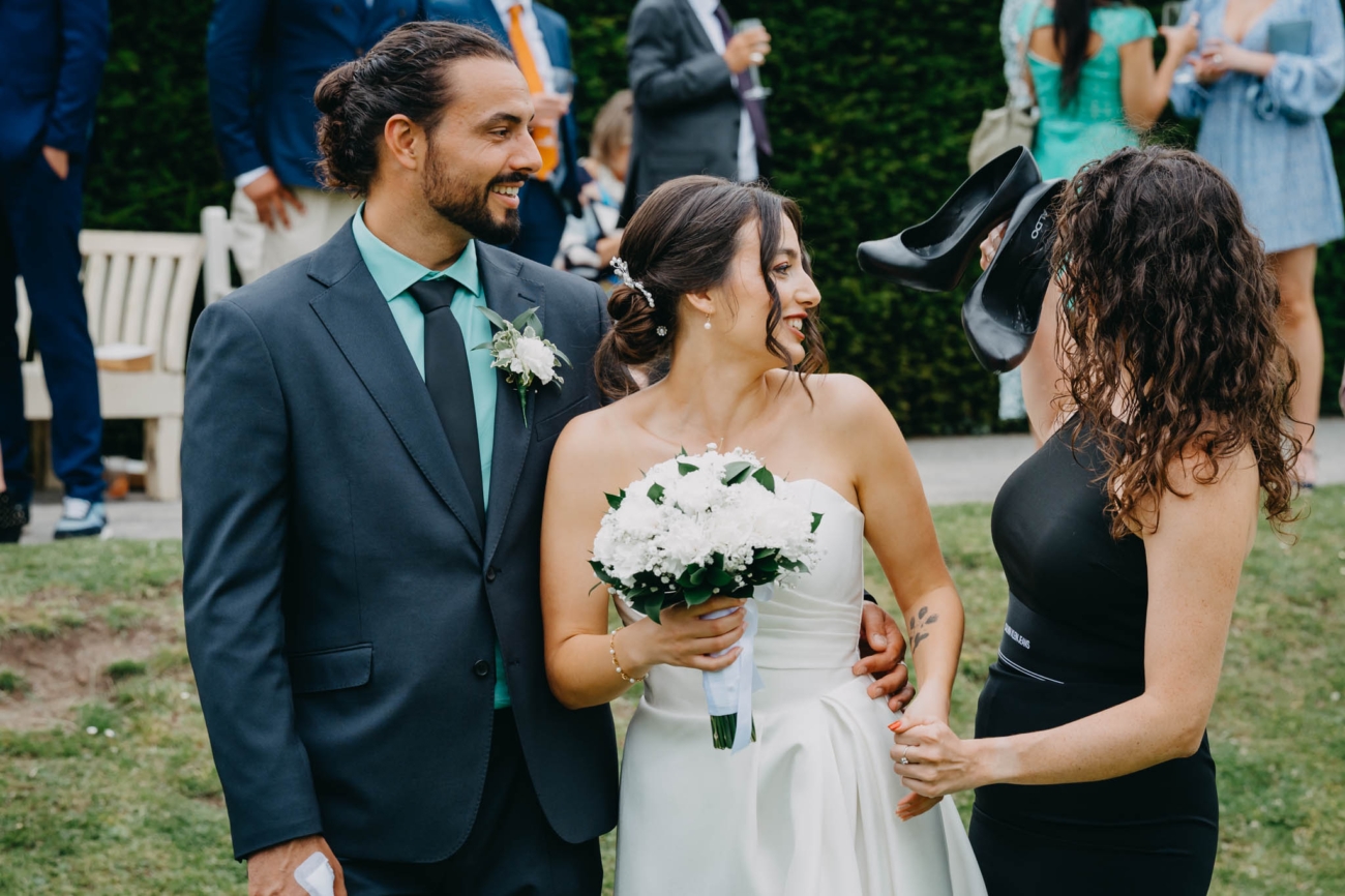 Wedding guest showing the bride a pair of high-heeled shoes as another guest smiles beside them