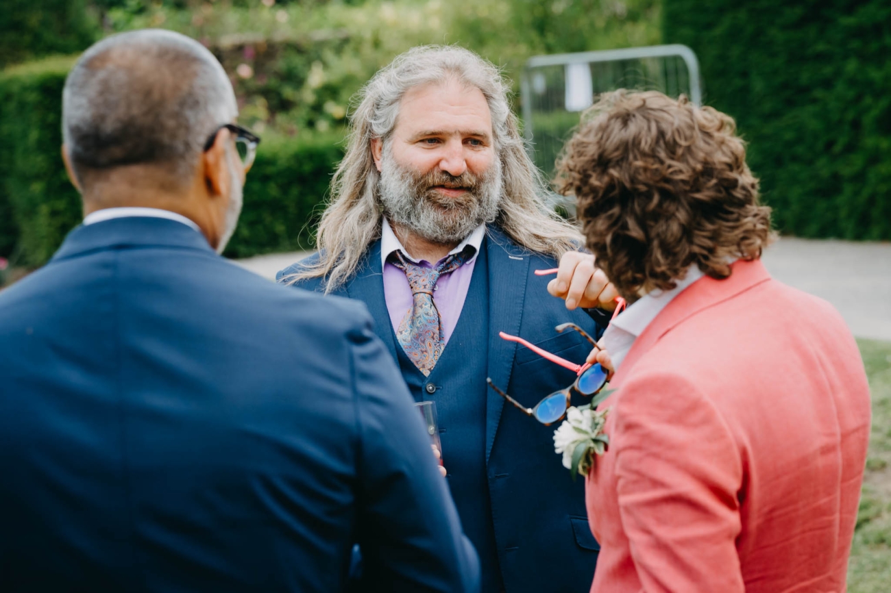 Three wedding guests chatting together during post-ceremony drinks in the gardens