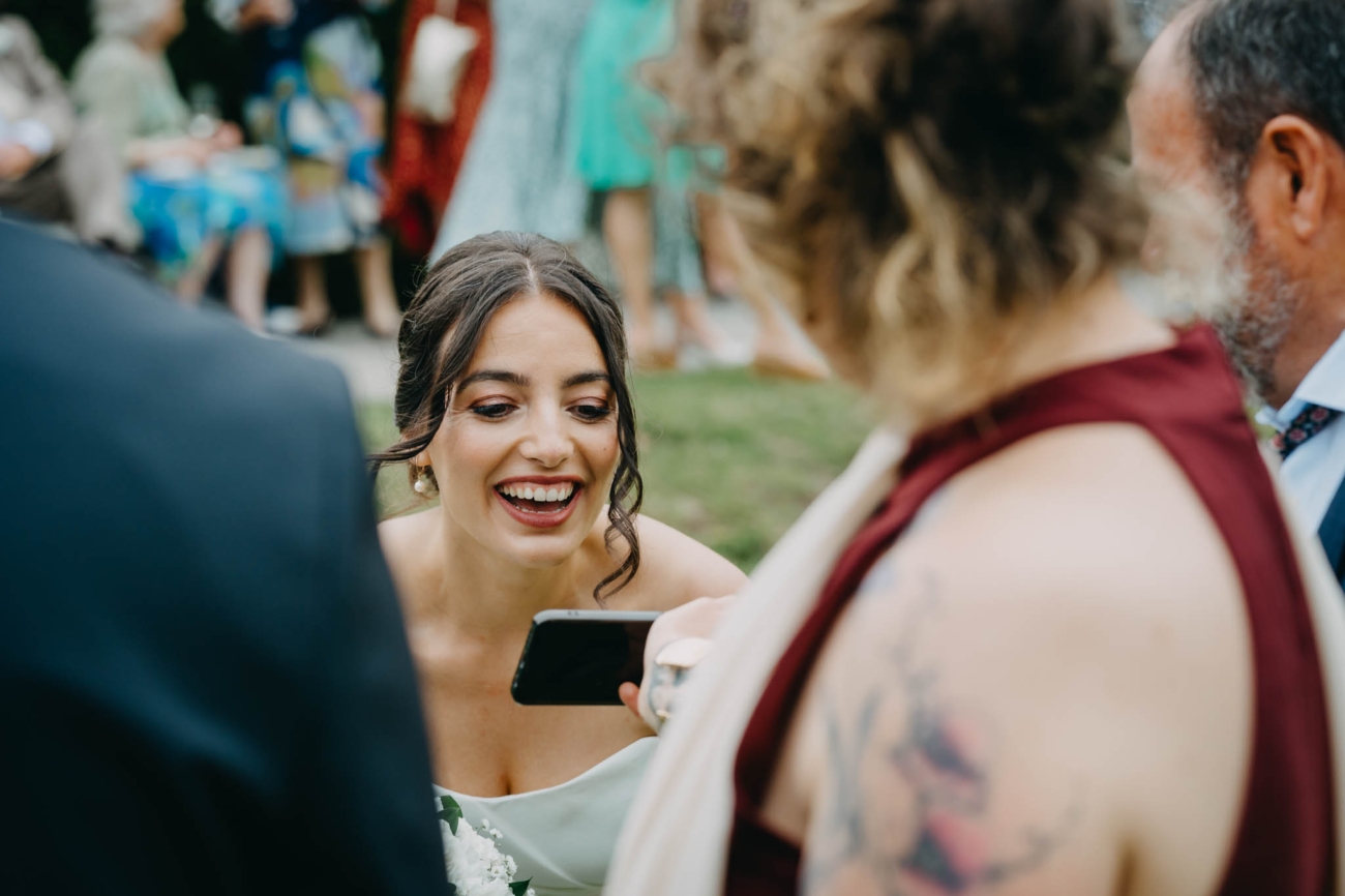 Bride laughing while looking at a mobile phone being shown to her by a wedding guest