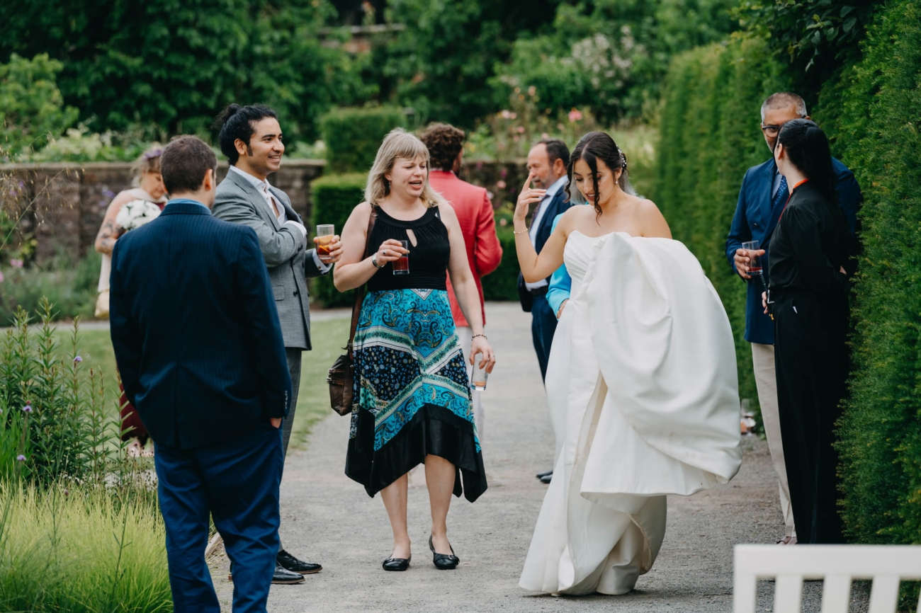 Bride carrying her dress as she walks among wedding guests in the Italian Gardens