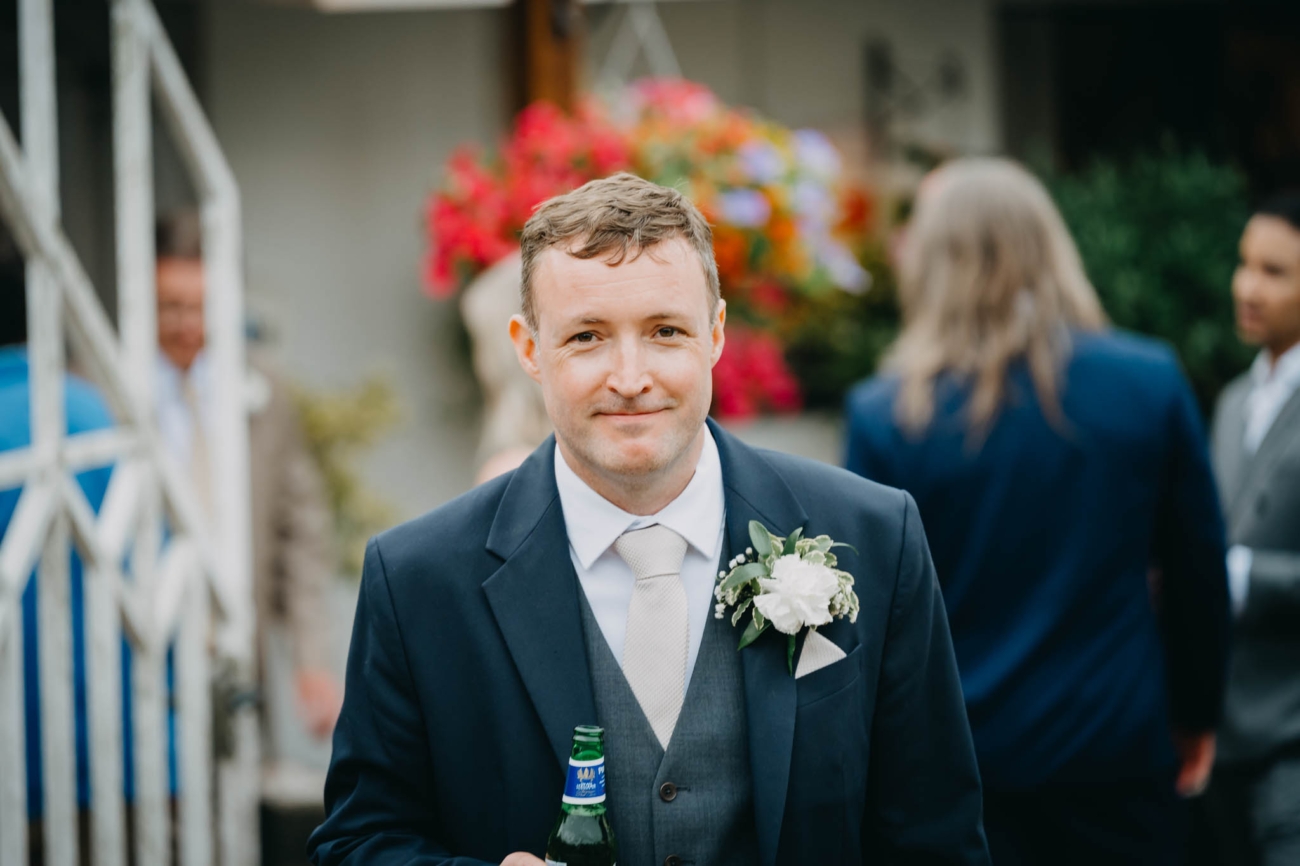 Groom holding a bottle of beer during the outdoor drinks reception at the Old Post House