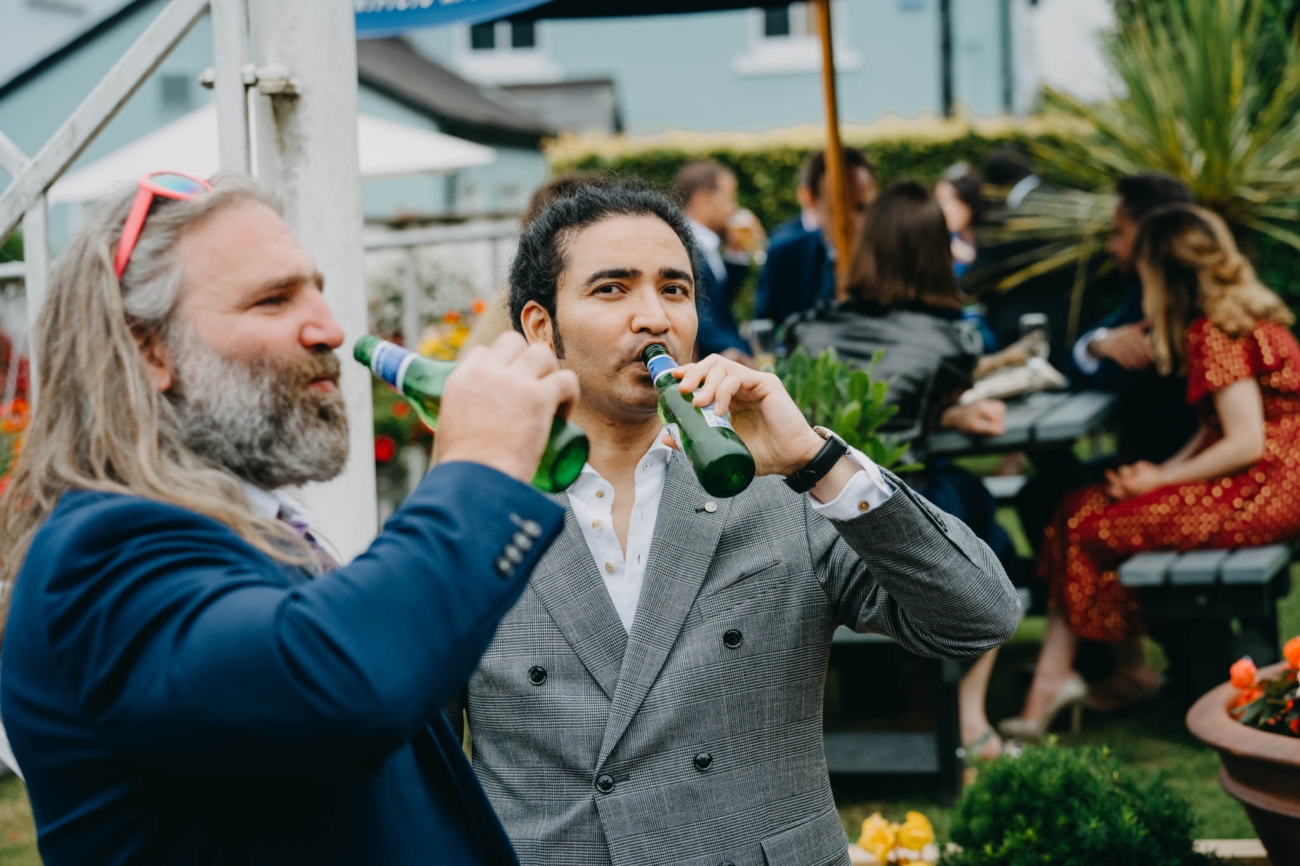 Two wedding guests drinking from beer bottles on the terrace at the Old Post House