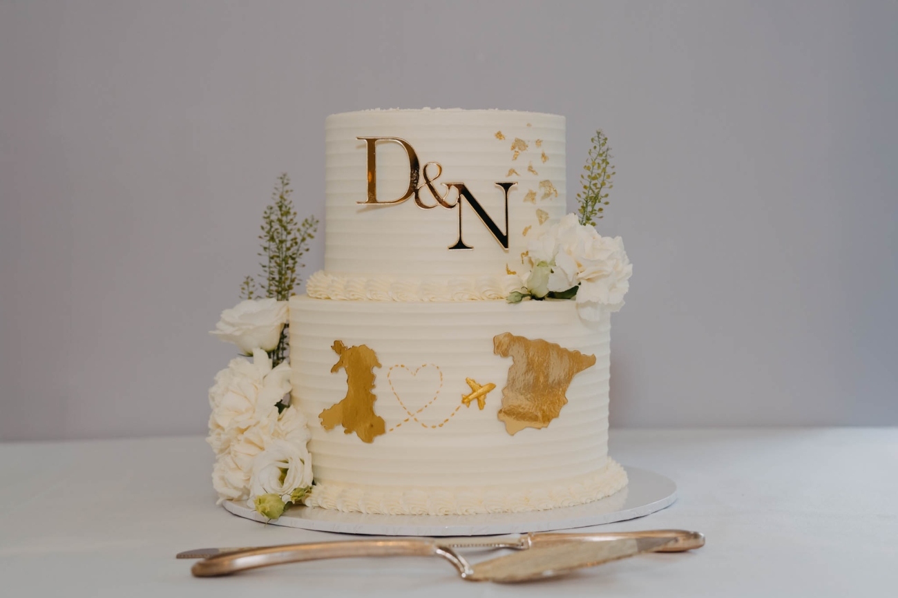 Two-tier white wedding cake decorated with gold map details and white flowers at the Old Post House