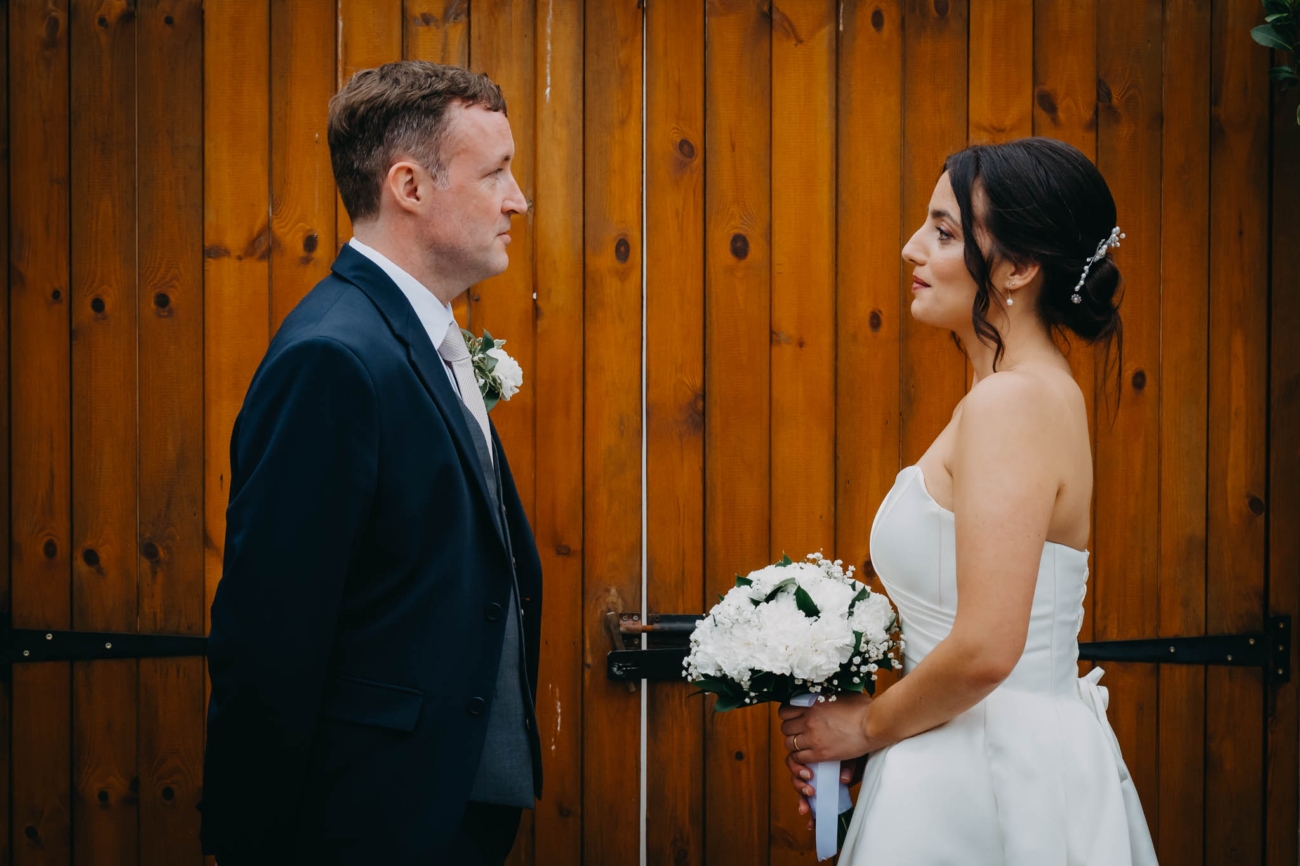 Bride and groom looking at each other in front of wooden doors at the Old Post House in St Fagans