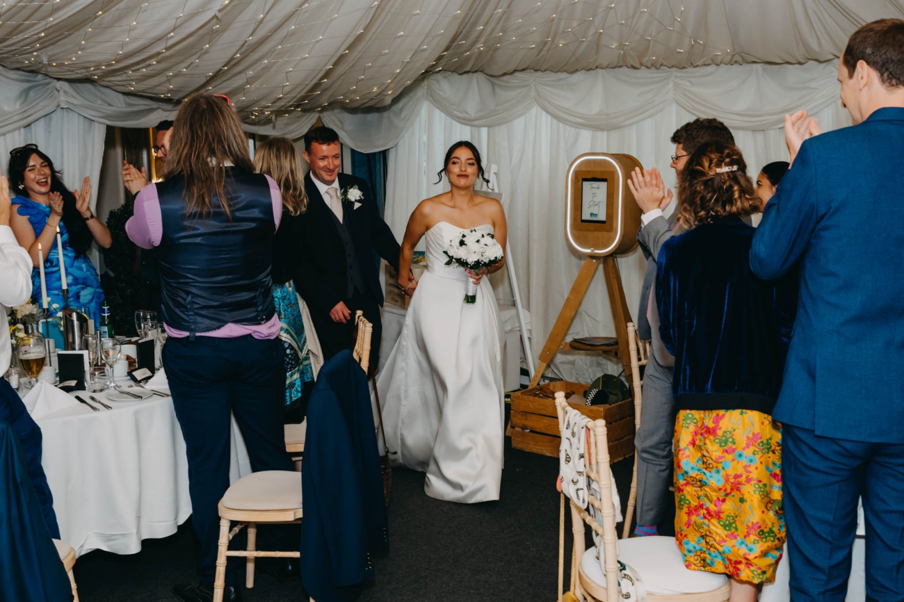 Bride and groom entering the Old Post House marquee as their wedding guests applaud