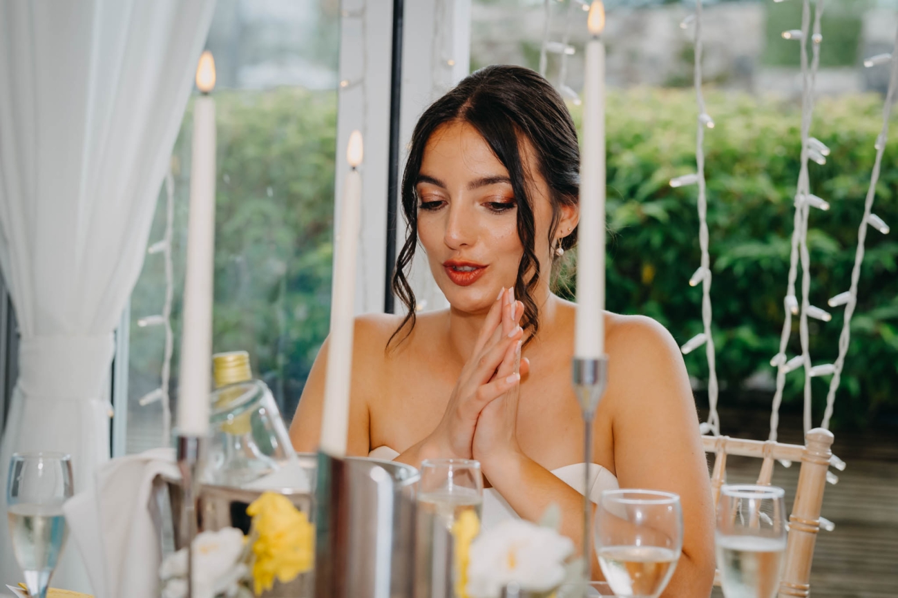 Bride gesturing as she talks at the top table during the wedding breakfast