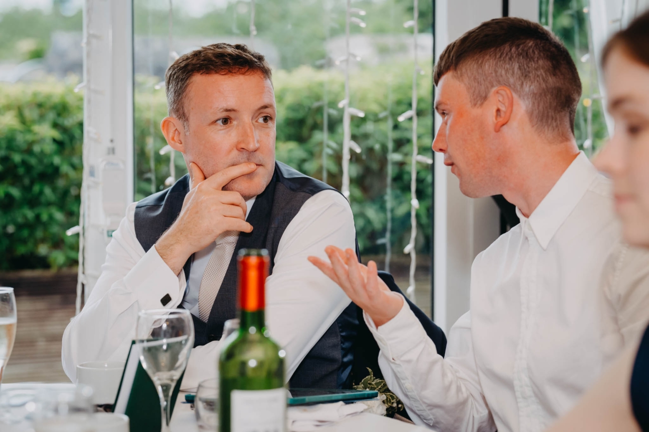 Groom listening as a wedding guest talks to him across the reception table