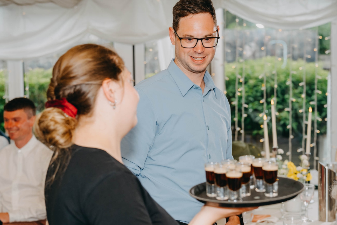Tray of shot glasses being carried through the wedding marquee as a guest smiles
