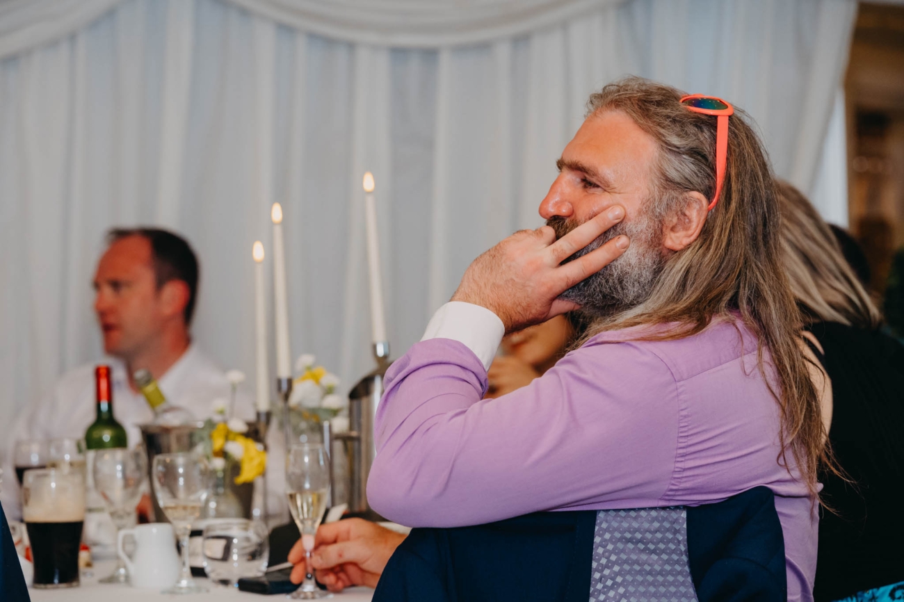 Long-haired wedding guest listening to the speeches with sunglasses resting on his head