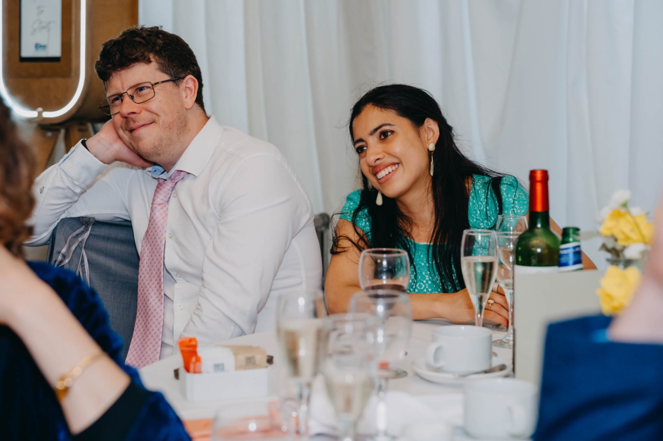 Two wedding guests smiling as they listen at their reception table