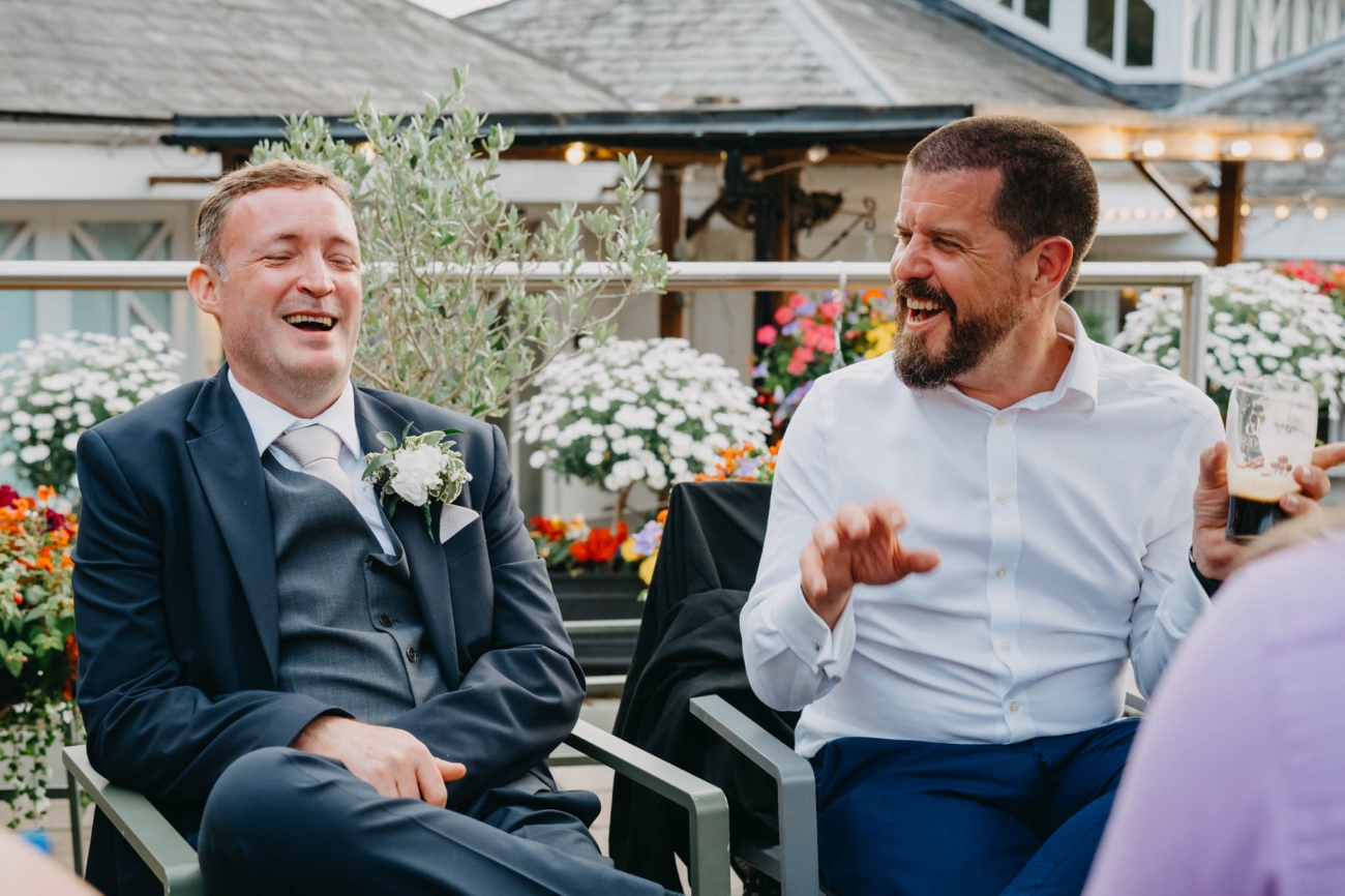 Groom laughing with a wedding guest on the Old Post House terrace