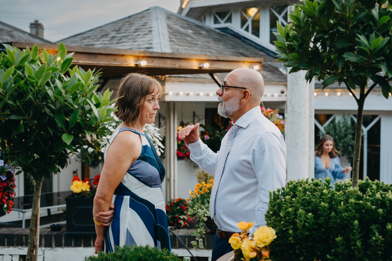 Two wedding guests talking beside colourful flowers on the Old Post House terrace