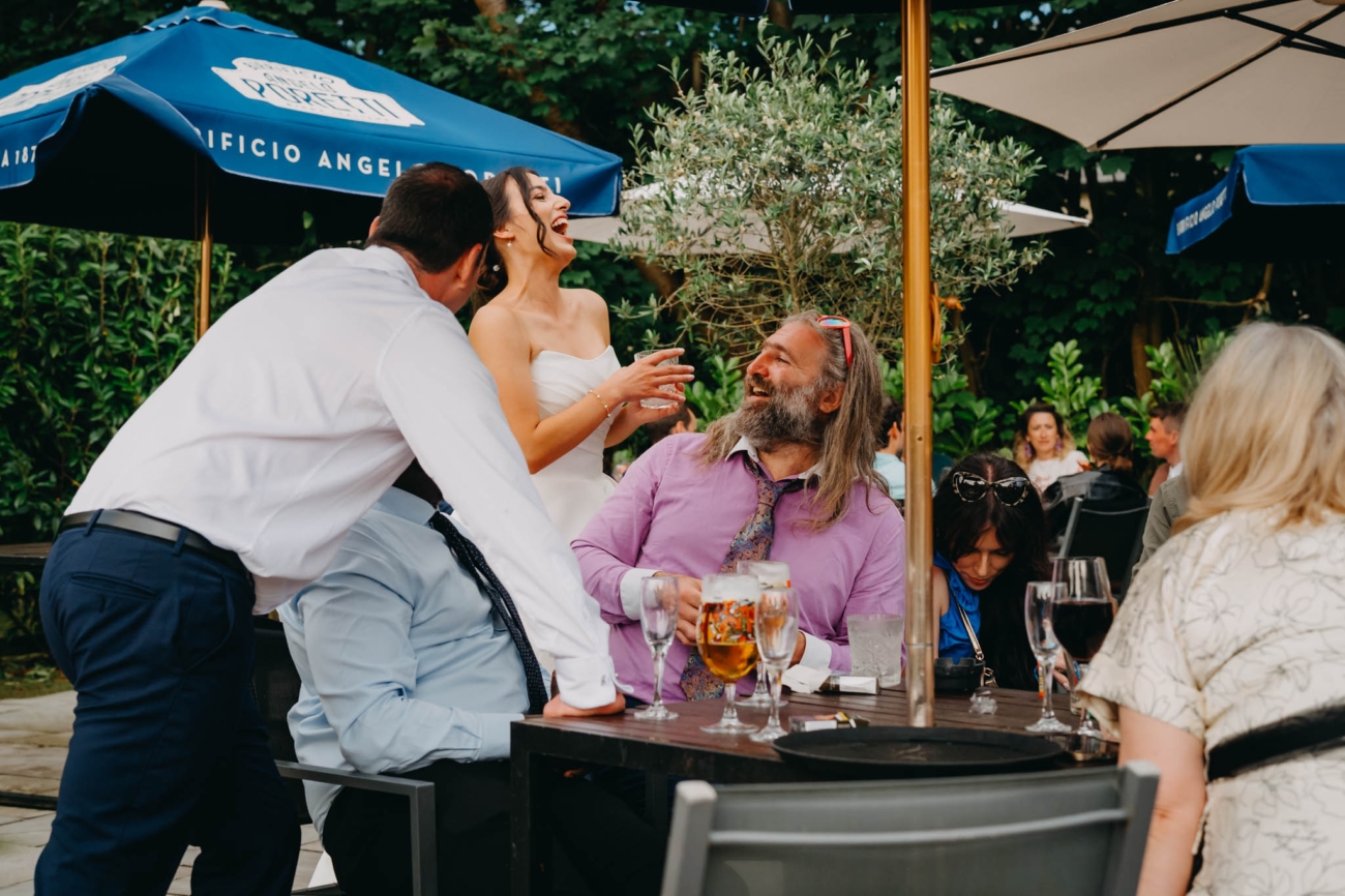 Bride laughing with wedding guests around an outdoor table on the terrace at the Old Post House in St Fagans